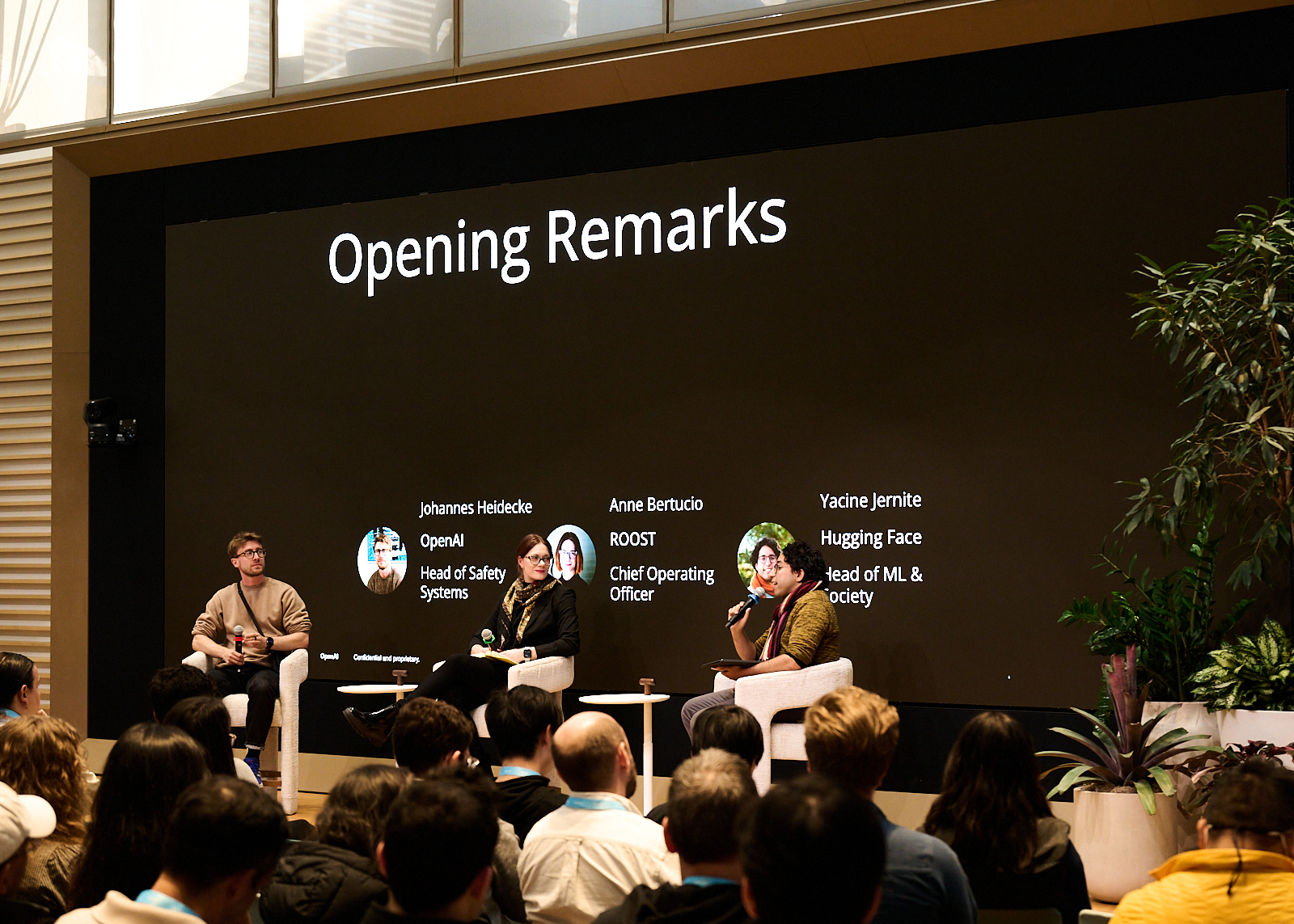 Three people sit on stage for a panel discussion with one holding a microphone. In white text on a black screen behind them: Johannes Heidecke, Head of Safety Systems at OpenAI, Anne Bertucio, Chief Operating Officer at ROOST, Yacine Jernite, Head of ML & Society at Hugging Face